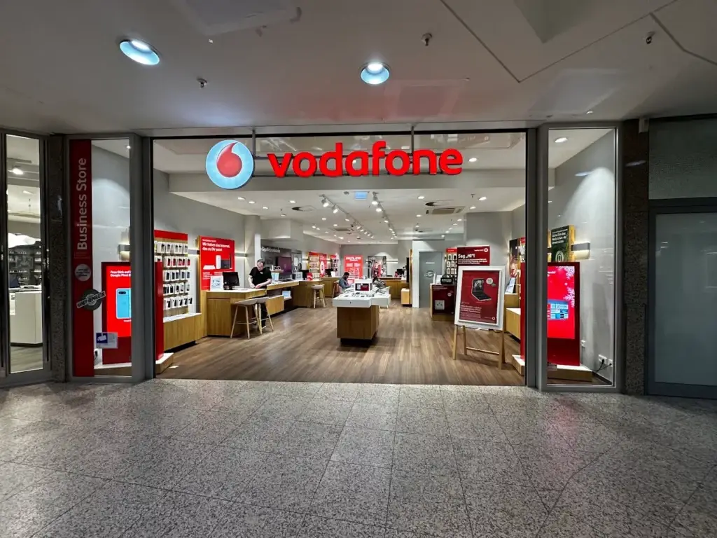 Eingang eines Vodafone Shops in einem Einkaufszentrum mit beleuchtetem Vodafone-Schriftzug